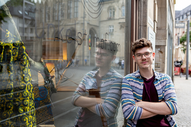 Vermutlich Mitarbeiter von IZUBA cothing lehnt an das Schaufenster des PopUp-Stores