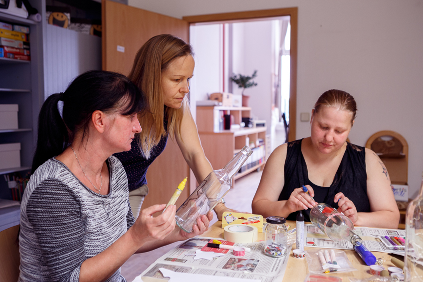 Drei Frauen bemalen Glasflaschen.