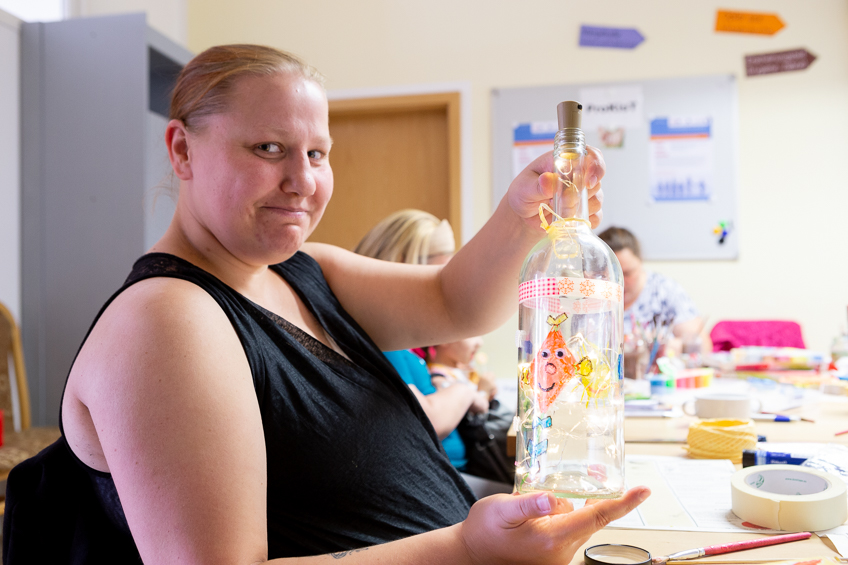 Eine Frau präsentiert ihre bemalte Flasche.