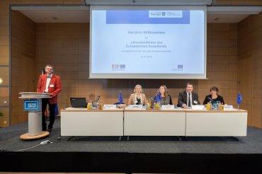Blick auf die Bühne mit unterschiedlichen Referenten und Präsentationsleinwand