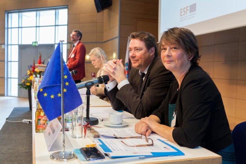 Diverse Speaker sitzend auf der Bühne vor einem Tisch