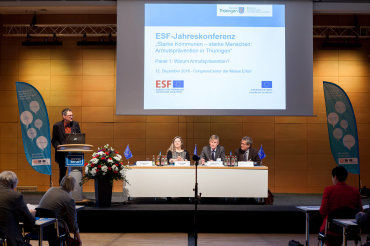 Blick auf die Bühne mit Redner und großem Präsentationschart im Hintergrund