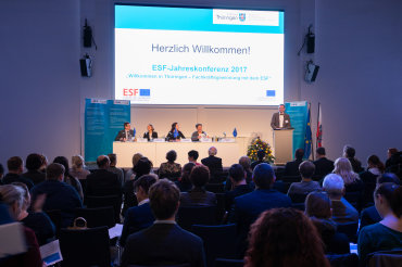 Blick aus Sicht des Publikums auf den Präsentationsbildschirm mit dem Begrüßungschart "Herzlich willkommen"