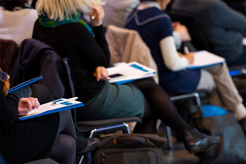 Veranstaltungsteilnehmer und Veranstaltungsteilnehmerinnen mit Informationsmaterial auf dem Schoß 